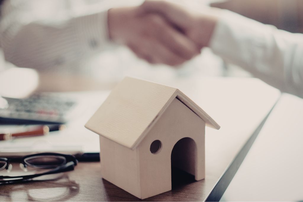 Handshake beside a house model illustrating professional insurance guidance